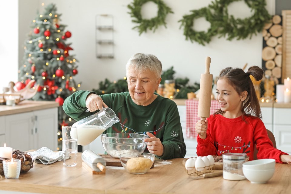 A grandmother and granddaughter baking beside a Christmas tree