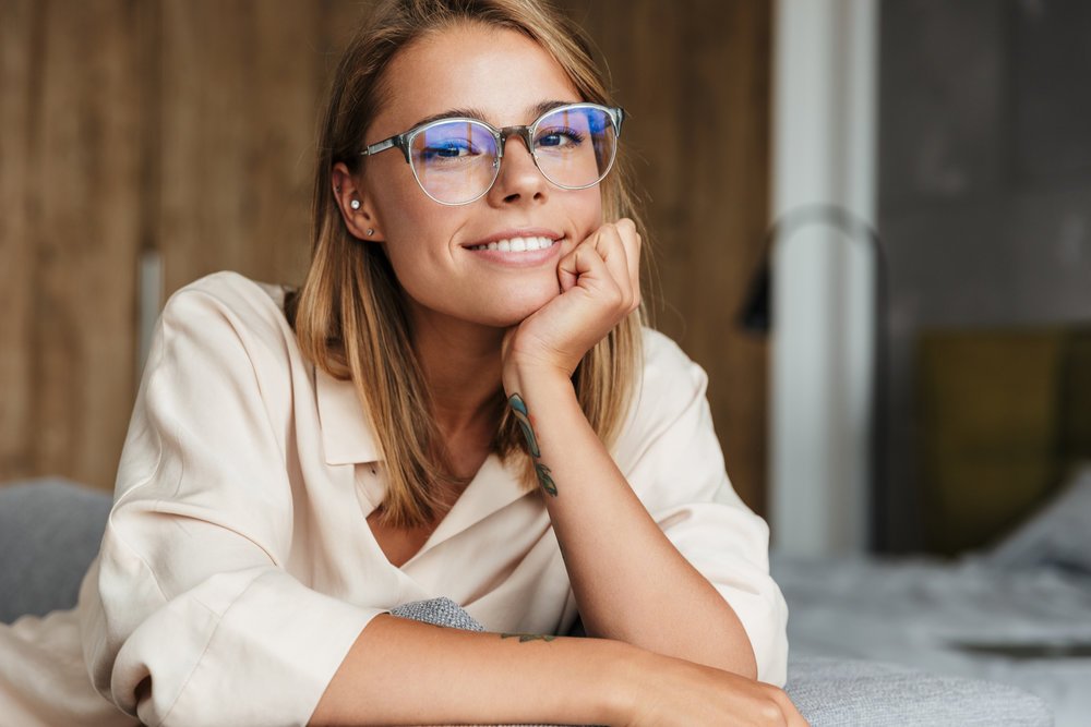 A woman in glasses resting her chin on her hand, smiling