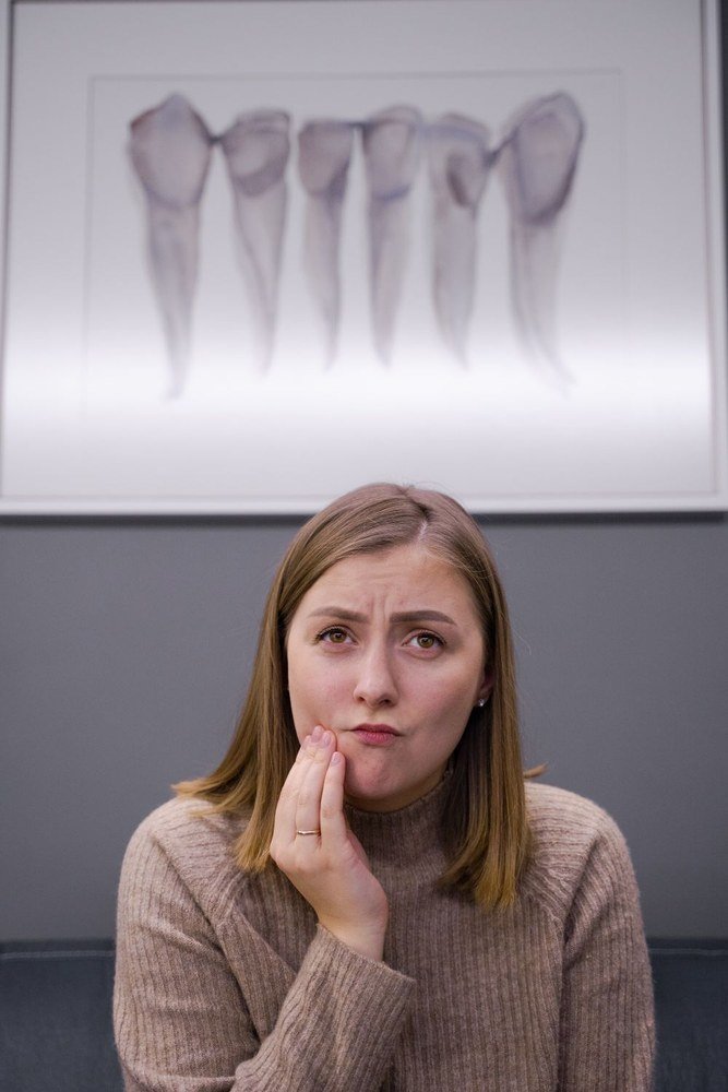 A woman holding her jaw in a dental office, tooth diagrams behind her