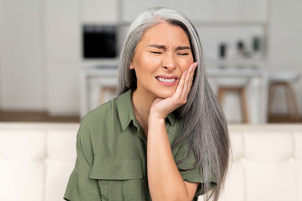 A woman wincing and holding her cheek in pain