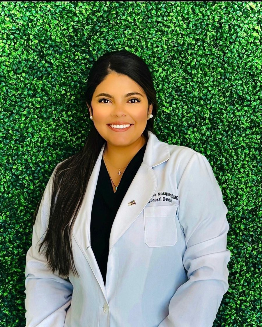 Dr. Fabiola Mosquera, DMD, in her white coat in front of a green wall