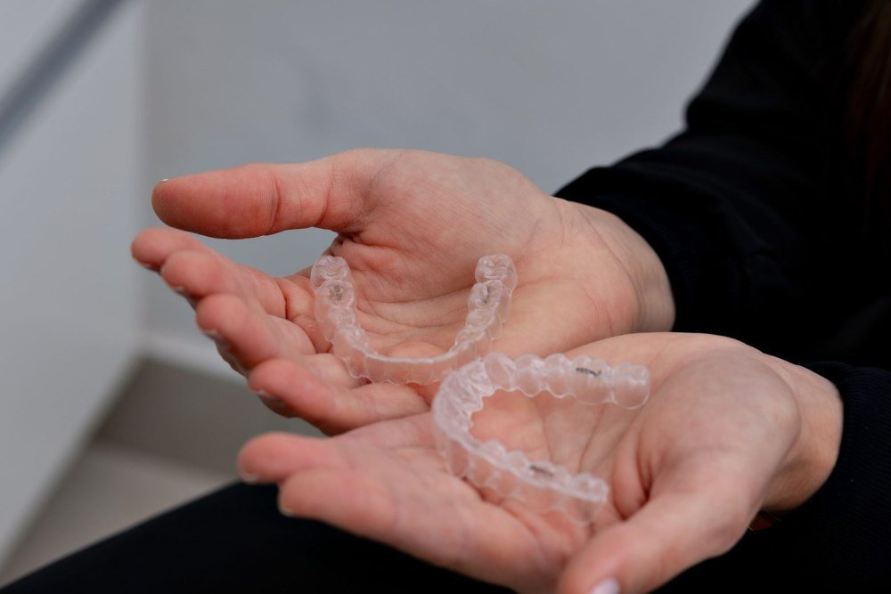 Open hands holding a pair of clear plastic aligner trays for the upper and lower teeth