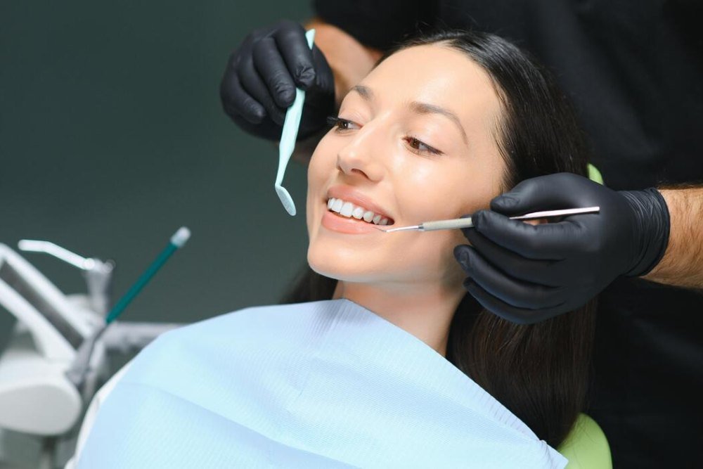 A smiling woman in the dental chair while a dentist checks her teeth