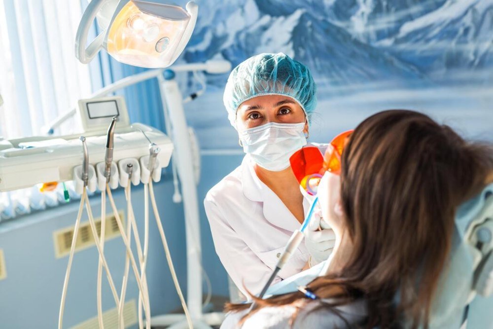 A dentist in a cap and mask attending to a patient in the chair
